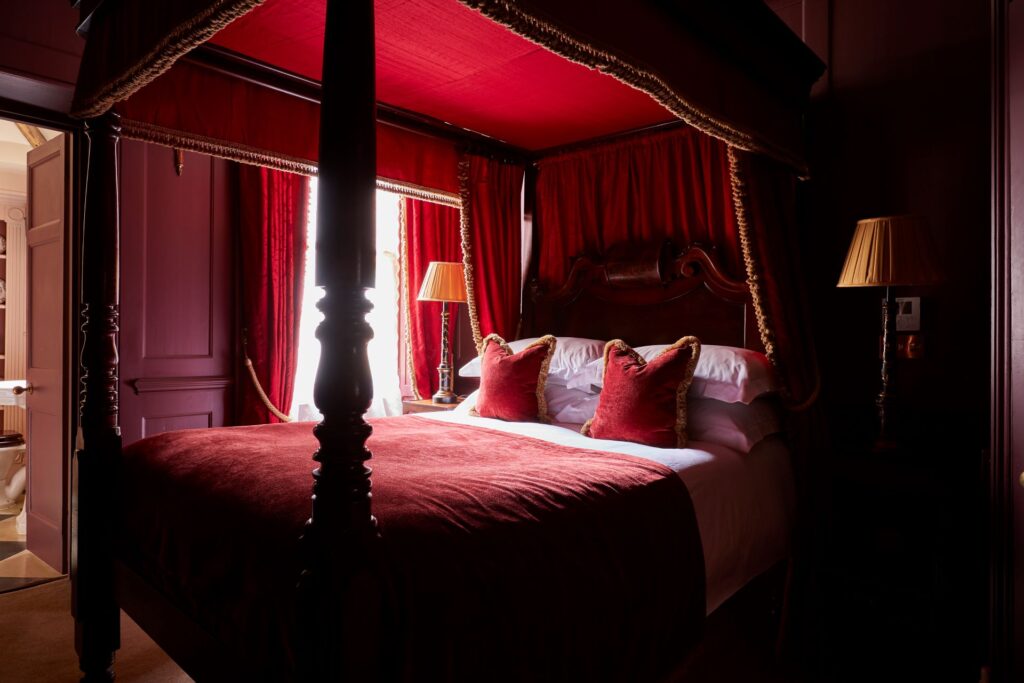 Four poster bed with red velvet throws and gold lampshades