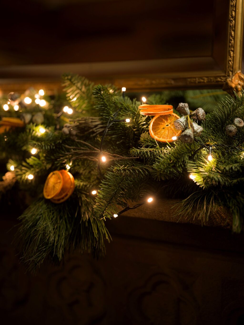 Close-up of a Christmas garland with pine branches, dried orange slices, berries, and warm fairy lights on a stone mantel at Hazlitt’s.