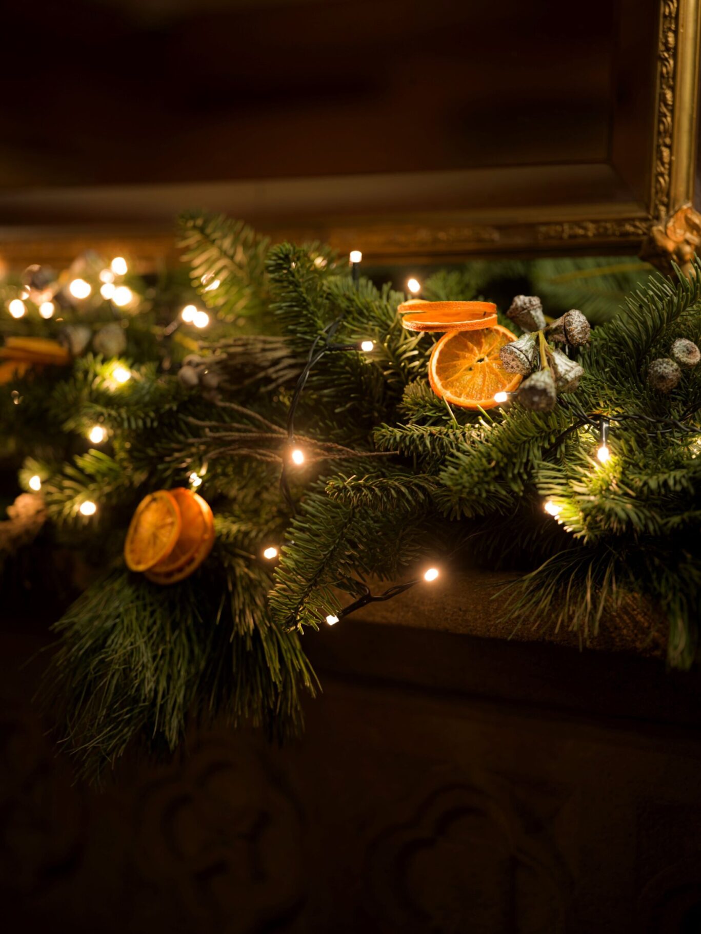 Close-up of a Christmas garland with pine branches, dried orange slices, berries, and warm fairy lights on a stone mantel at Hazlitt’s.