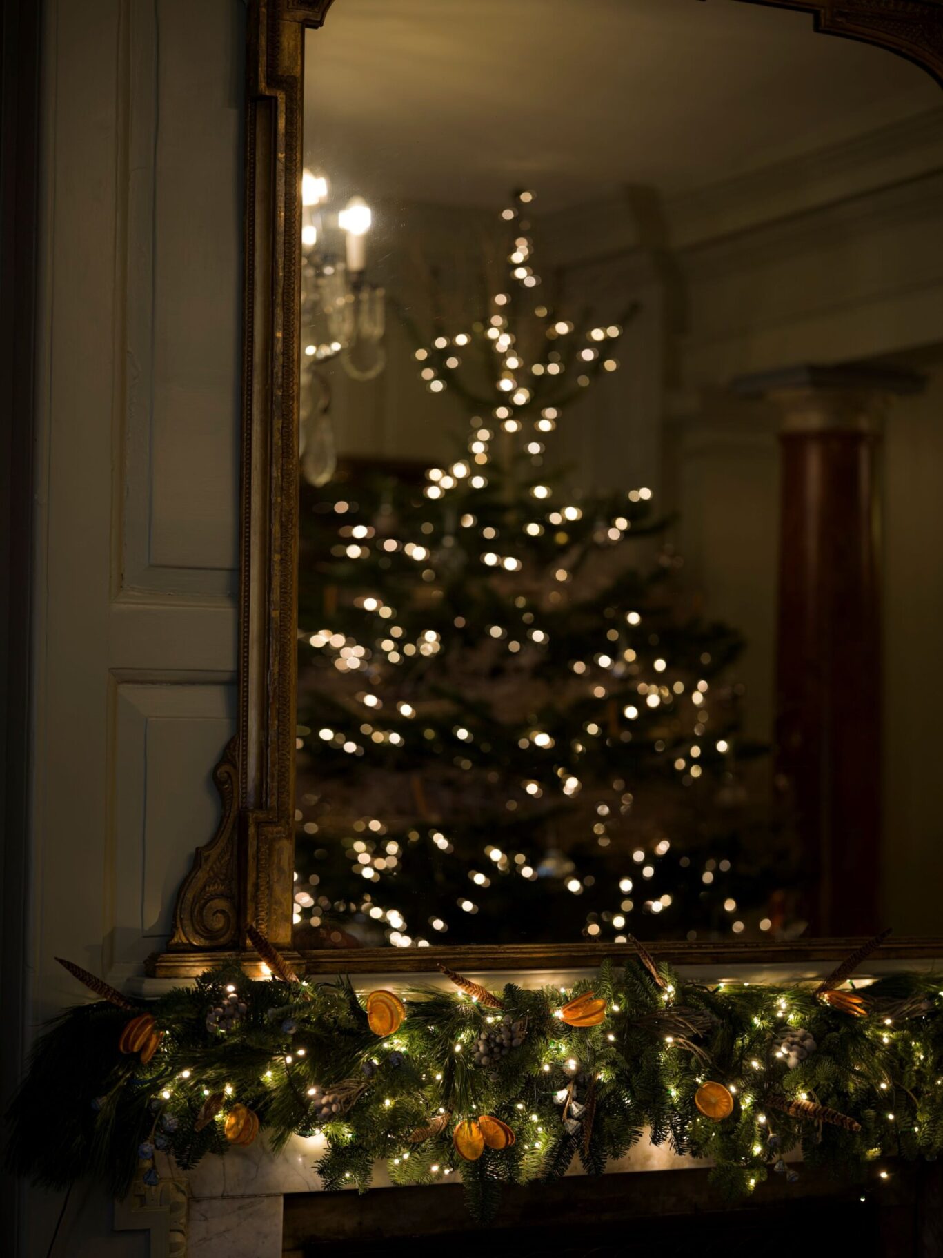 A mirror above a decorated mantel reflects a softly lit Christmas tree and chandelier at Hazlitt’s.