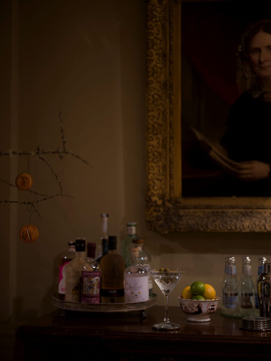 The Gin Bar at Hazlitt’s with spirits, a martini glass, citrus bowl, and a portrait in a gold frame above.